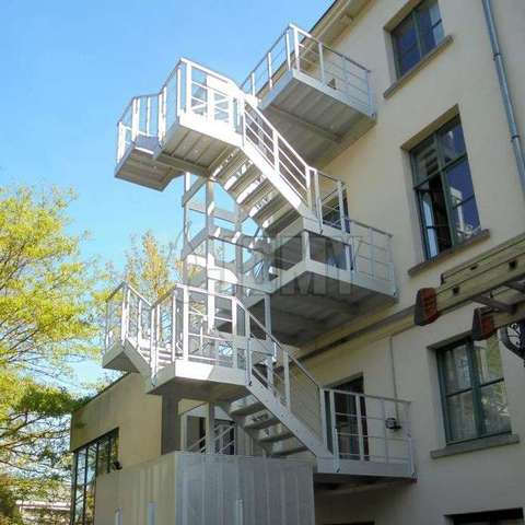 Escaliers extérieurs d'évacuation et d'accès Escaliers en aluminium pour l'évacuation de secours et pour l'accès, placés à l'extérieur d'un bâtiment de taille moyenne.
